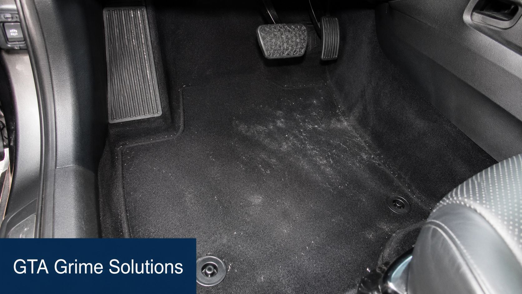 A clean black car footwell area with floor mats and pedals inside a vehicle interior.