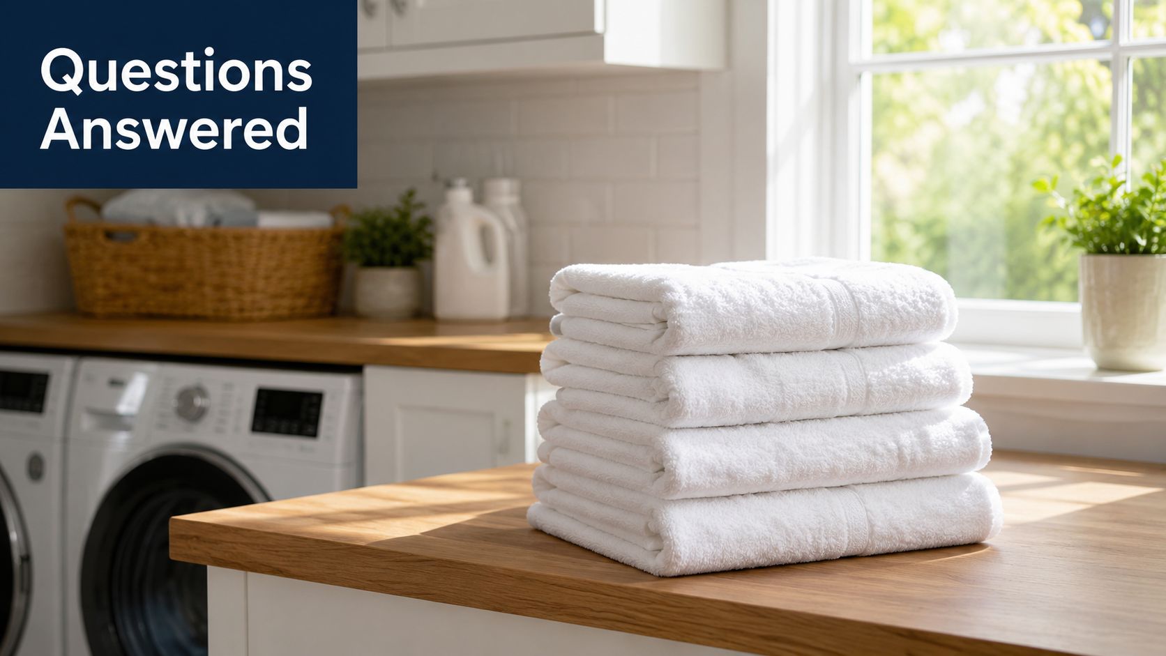 A stack of clean, folded white towels sits on a wooden counter in a bright laundry room.