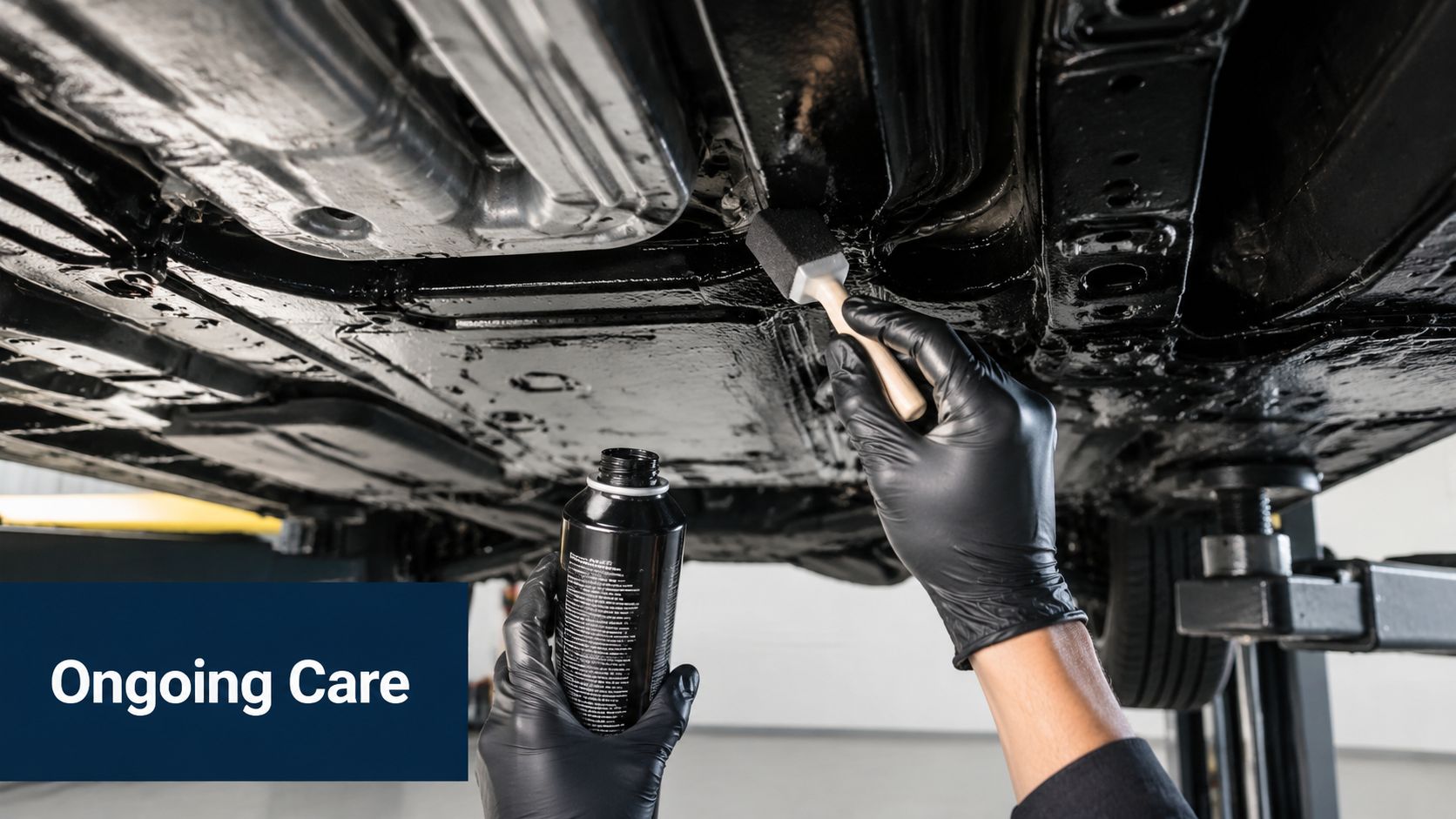 A mechanic wearing black gloves applying protective sealant to a vehicle underbody with a foam brush.