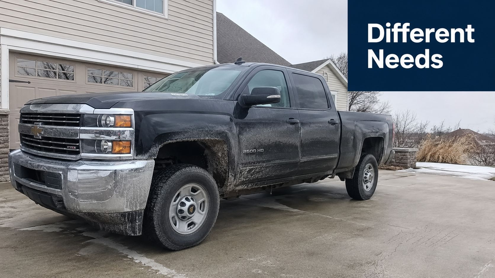 A dirty black Chevrolet 2500 HD pickup truck parked on a concrete driveway in front of a house.