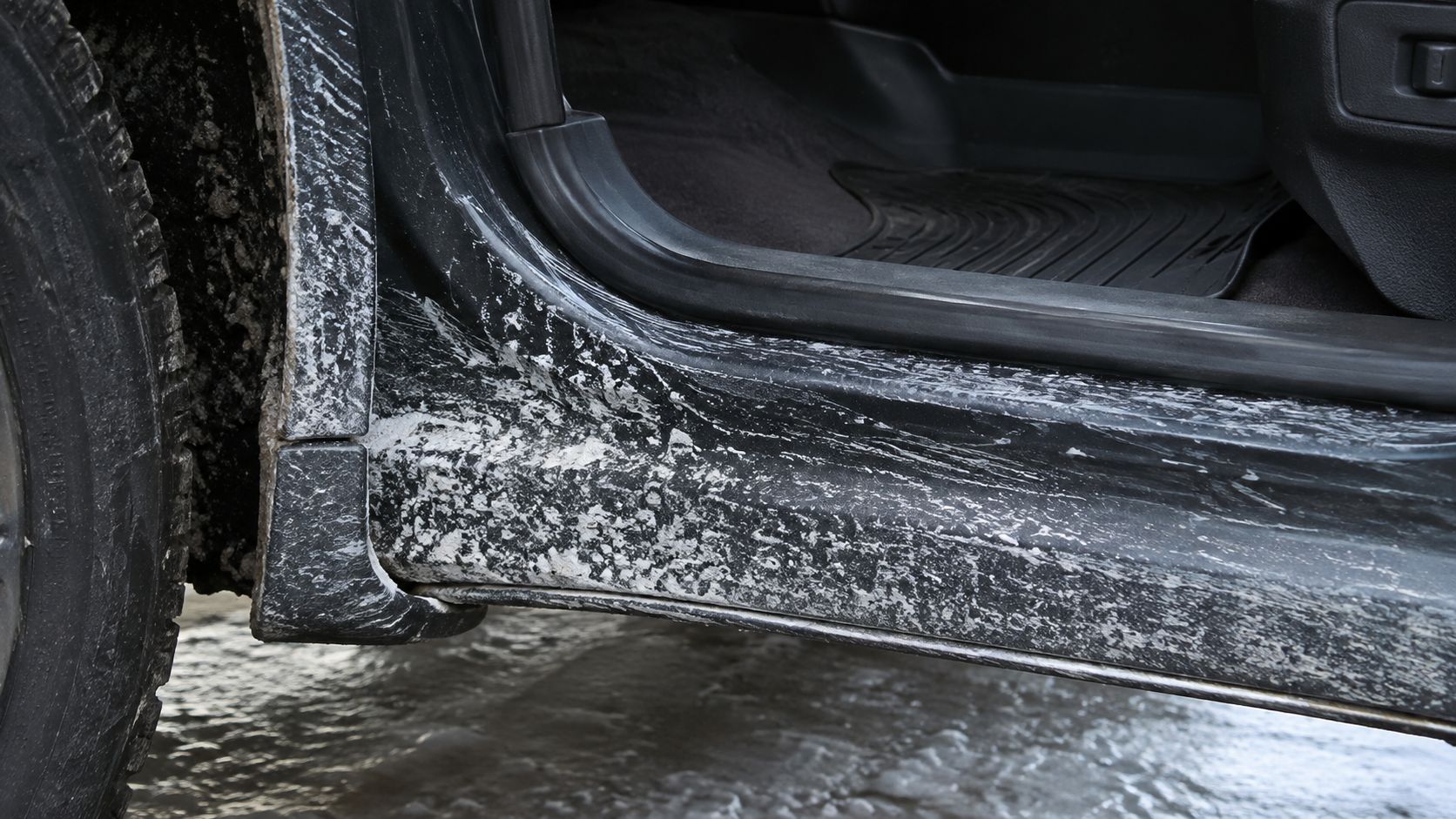 A close up view of a vehicle rocker panel heavily covered in dried road salt stains.