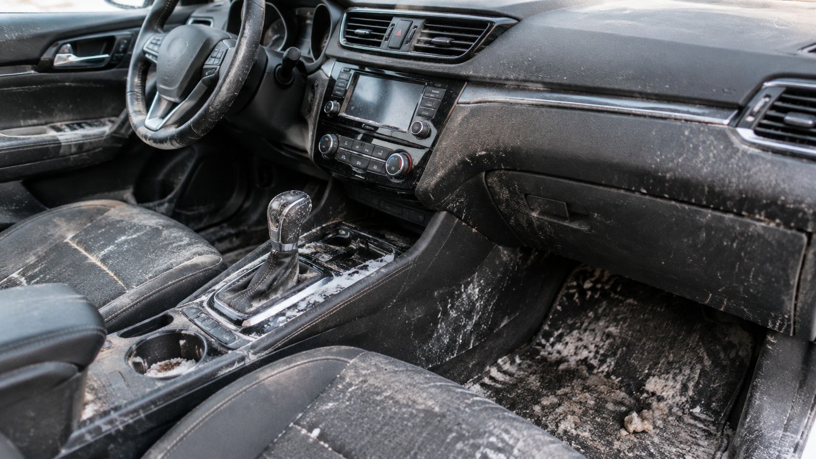 A very dirty car interior covered in mud, salt, and debris, needing professional interior cleaning services.