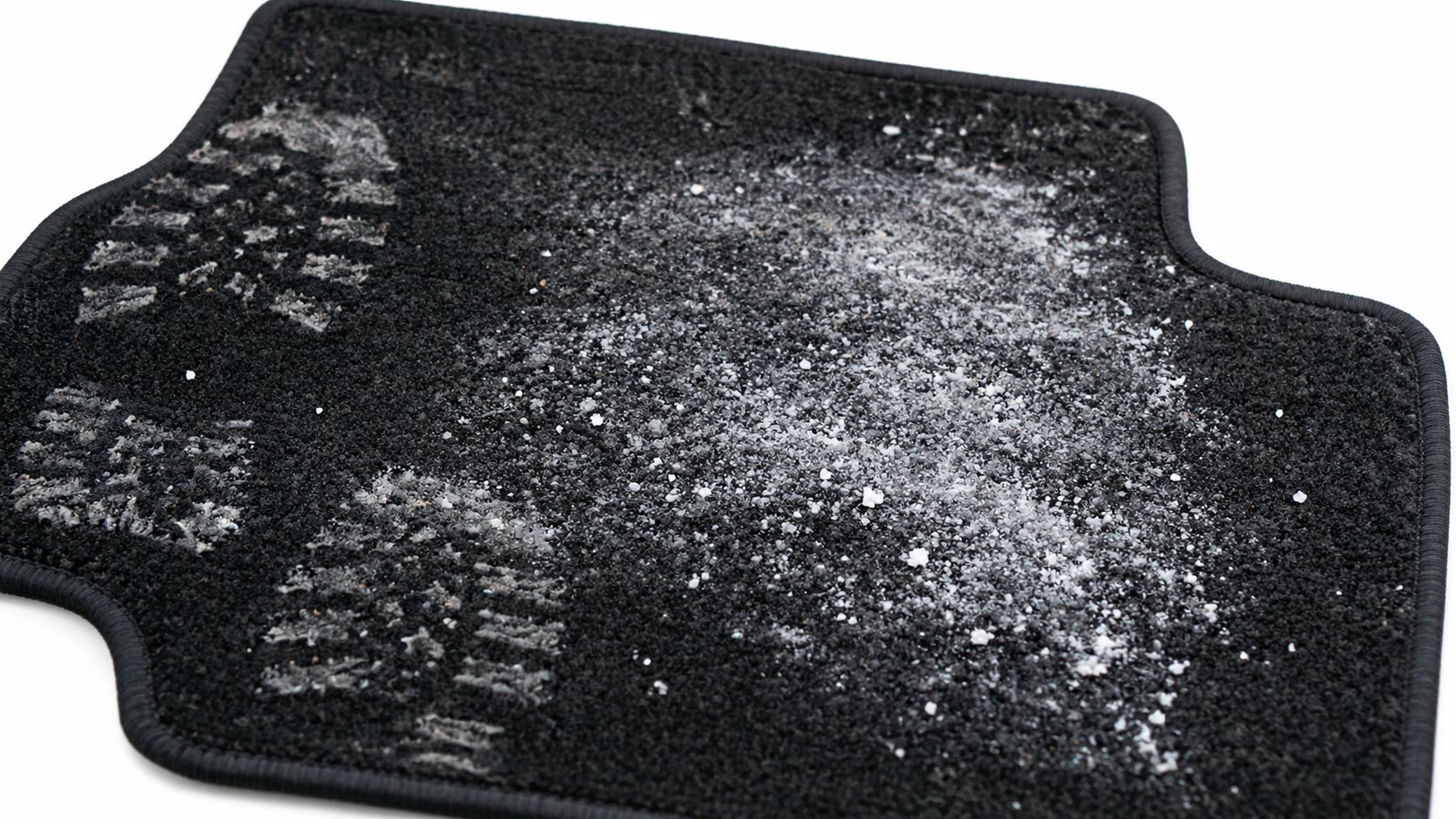 A dirty black car floor mat covered with salt stains and footprints from snowy winter boots.
