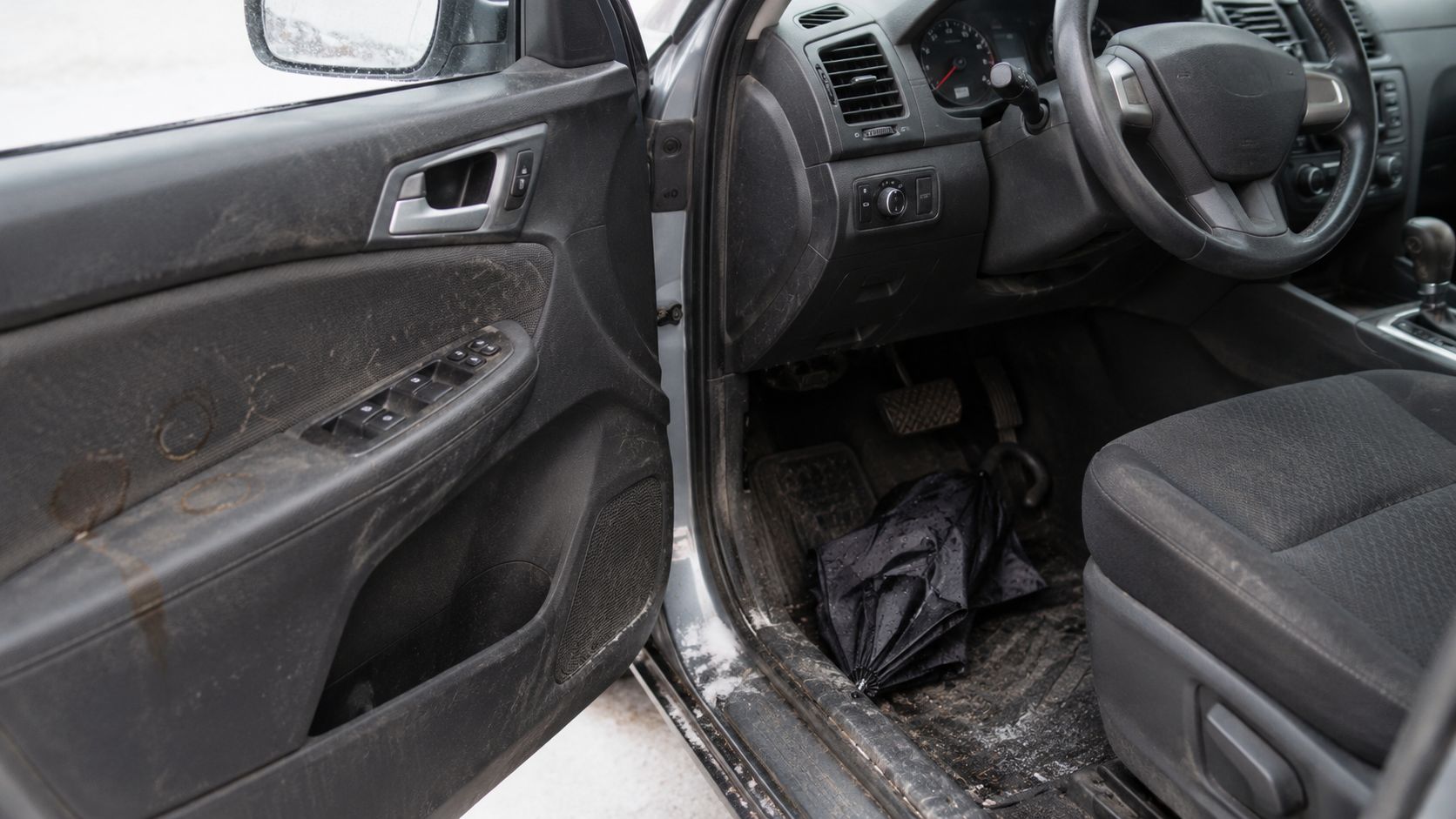 A dirty and messy interior of a vehicle with mud stains on the door and an umbrella on the floor.
