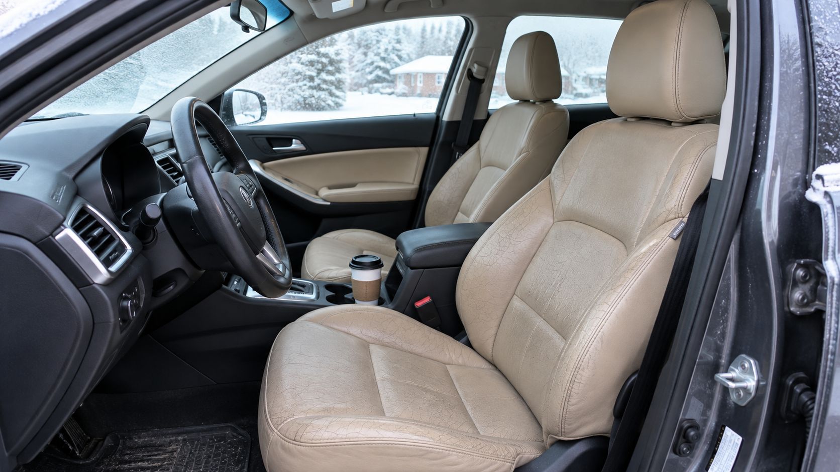 A view of a car interior featuring worn tan leather seats and a cup holder with coffee.